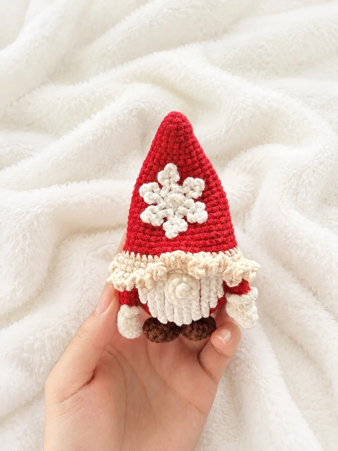 Crochet gnome with a tall red snowflake hat, cream beard and brown shoes resting in a hand