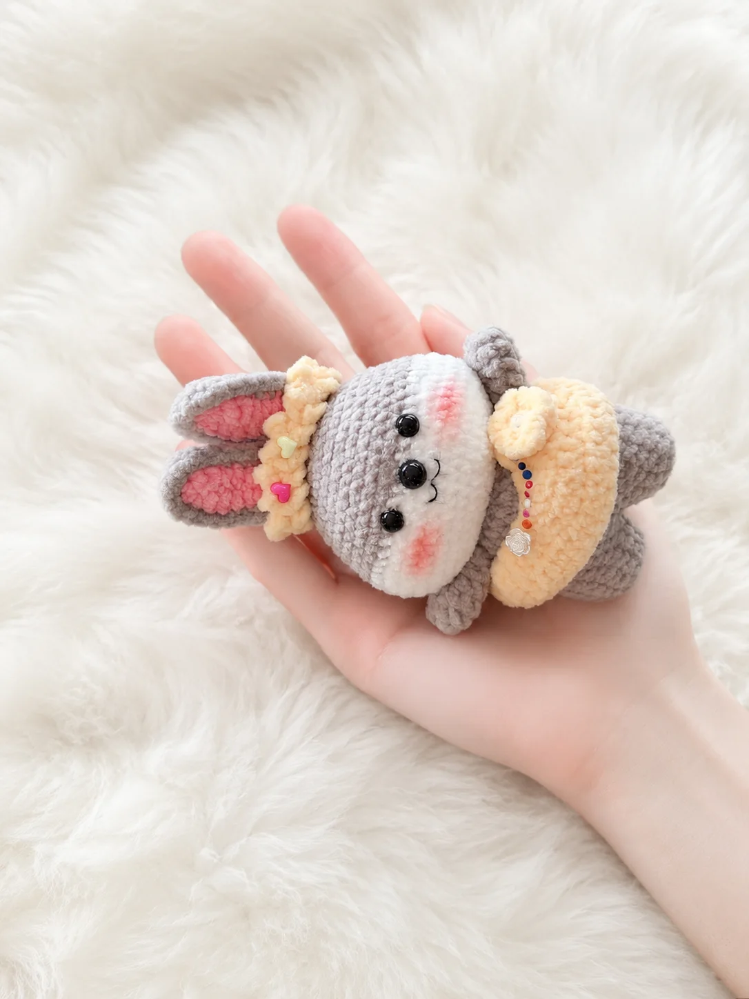 Grey crochet bunny in a buttercup-yellow dress and a matching decorative headband with heart-shaped beads, resting in a hand