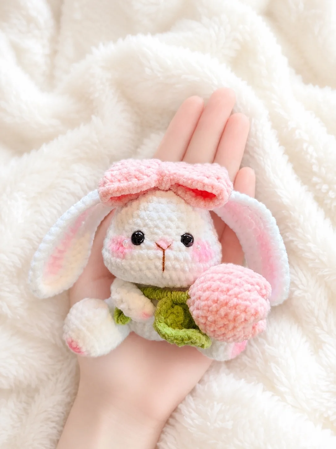 White crochet bunny with a pink bow and pink tulip resting in a hand