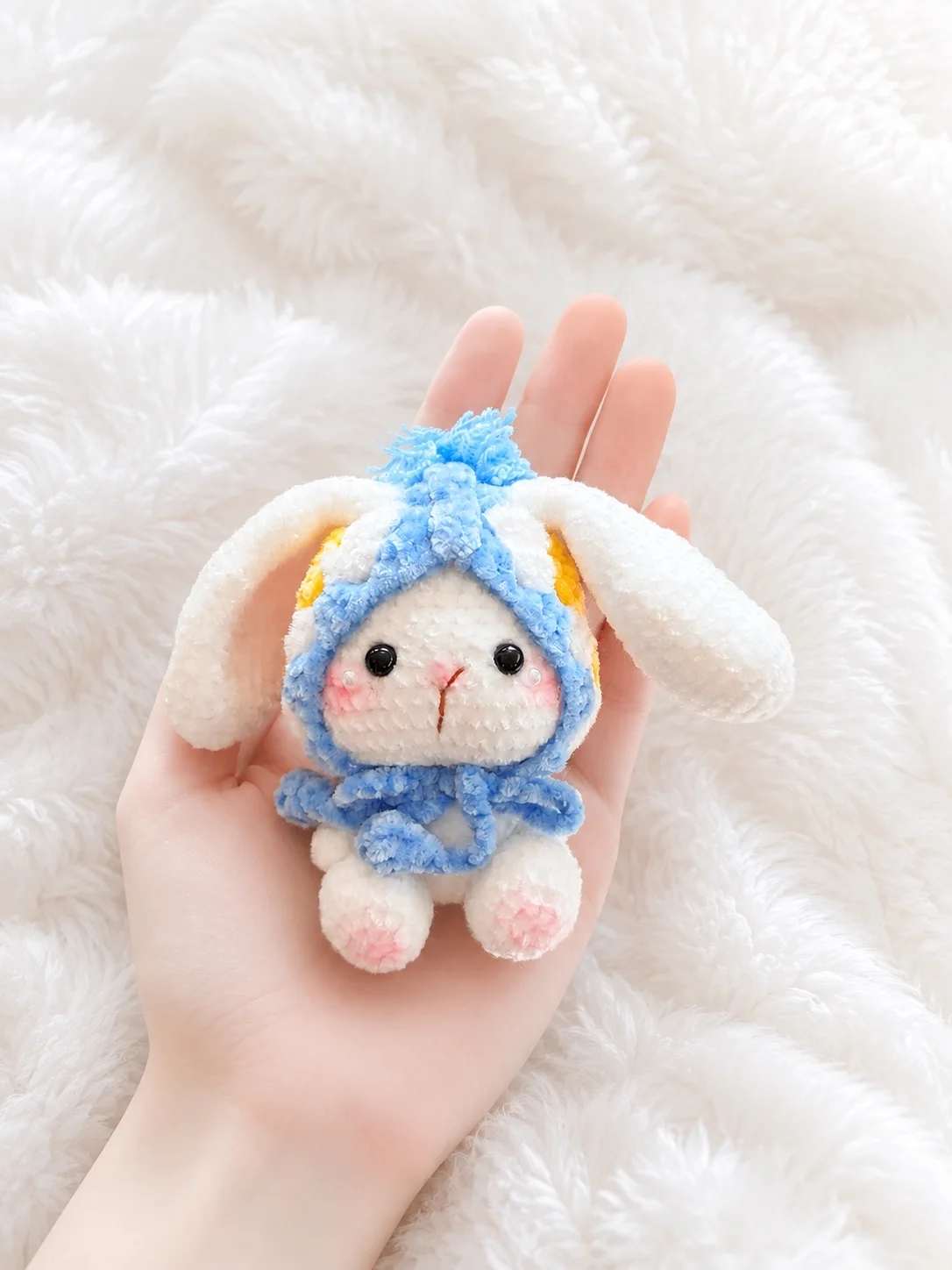 White crochet bunny wearing a pale blue flower bonnet, resting in a hand
